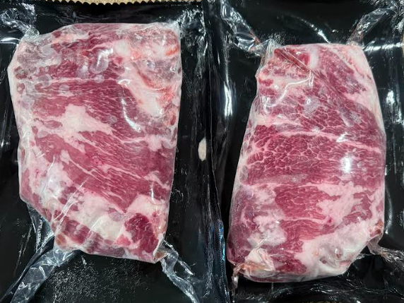Jake+Moore+-+Screenshot+2026-01-15+145347 Two vacuum-sealed packages of marbled beef steaks, showcasing rich red and white fat distribution, ideal for grilling or slow cooking.