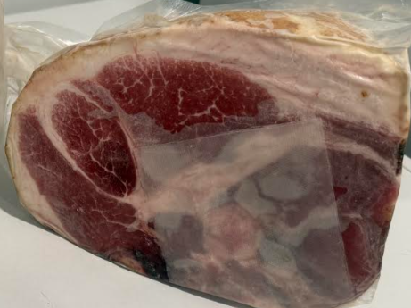 Jake+Moore+-+Screenshot+2026-01-15+145433 (1) A cured meat product, specifically a large piece of ham, wrapped in plastic packaging, showcasing marbled fat and rich red meat. Ideal for gourmet dishes and charcuterie boards.